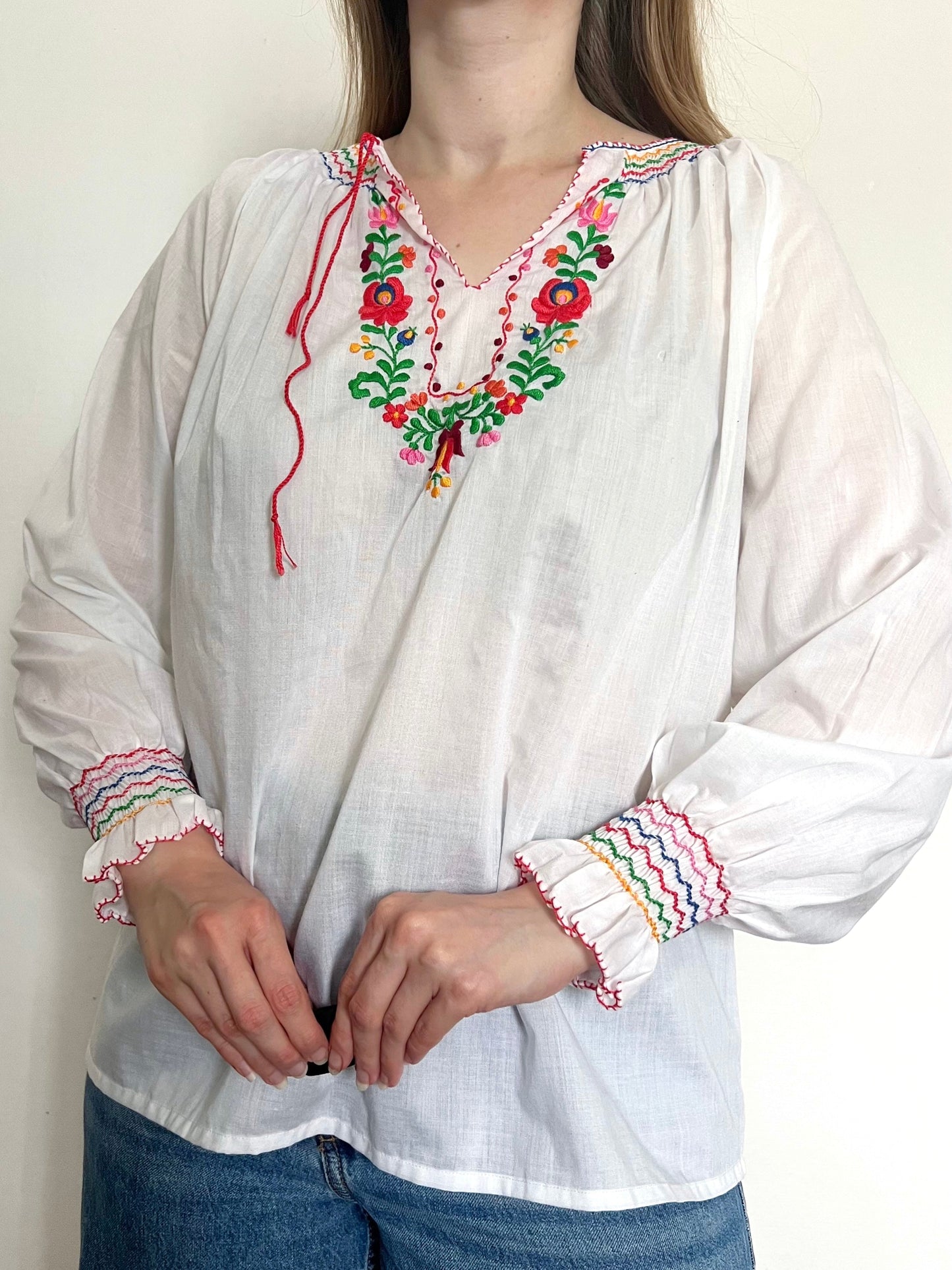 White blouse with colorful embroidery and cuffs worn by a person against a plain background