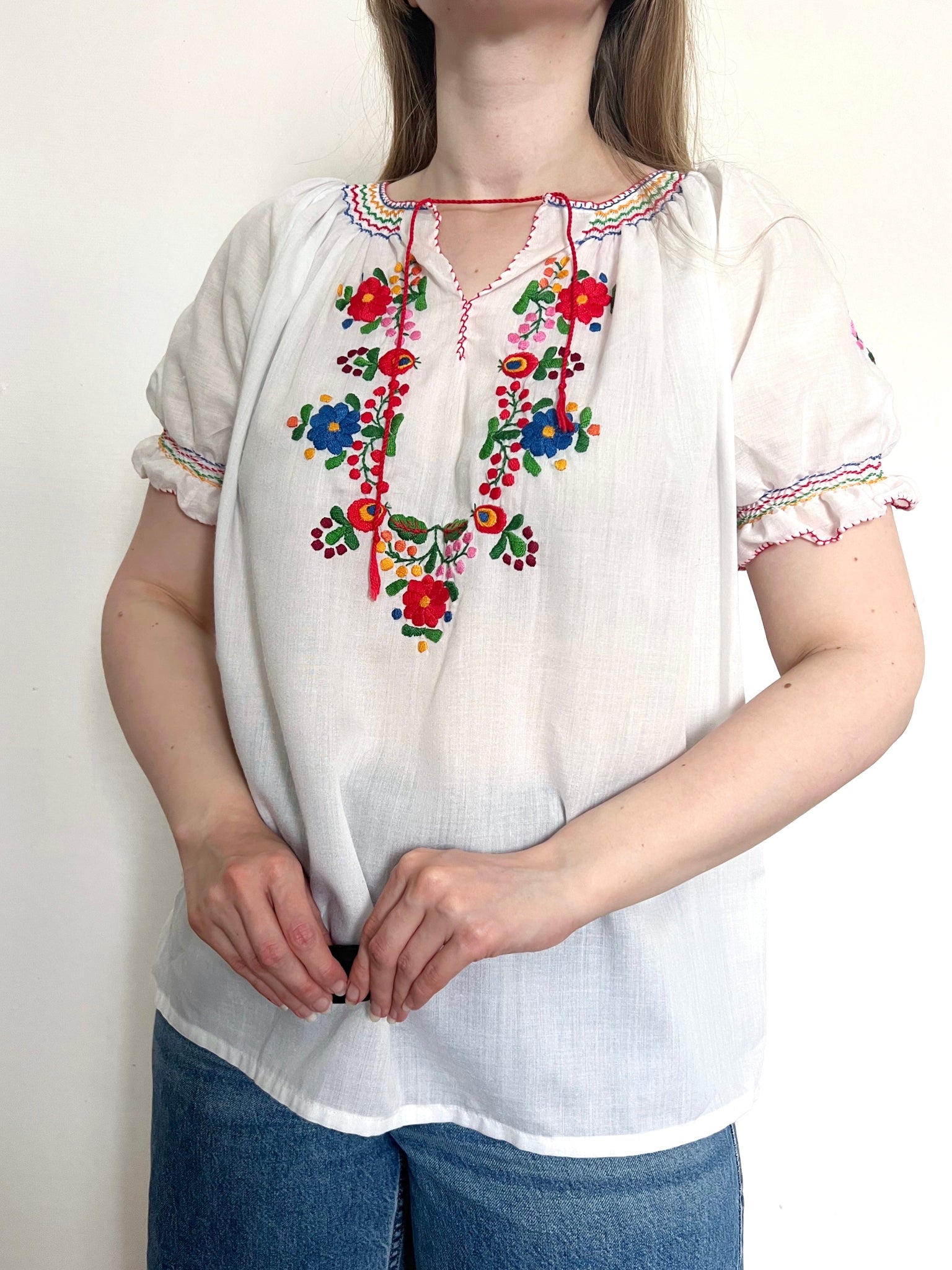 White blouse with colorful embroidery worn by a person on a plain background