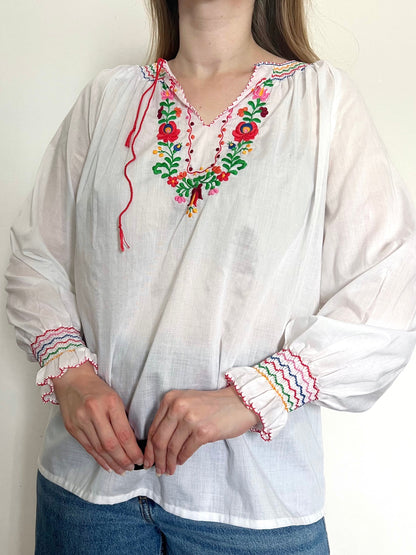 White blouse with colorful embroidery and cuffs worn by a person against a plain background