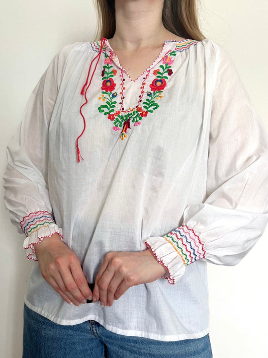 White blouse with colorful embroidery and cuffs worn by a person against a plain background