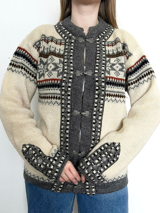 A wool cardigan in a classic Nordic/Norweigan pattern, mainly in gray and white. Has buttons on the sleeves. Made in Norway.