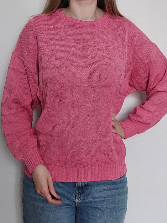 A person wearing pink knitted sweater with unique swirly pattern 