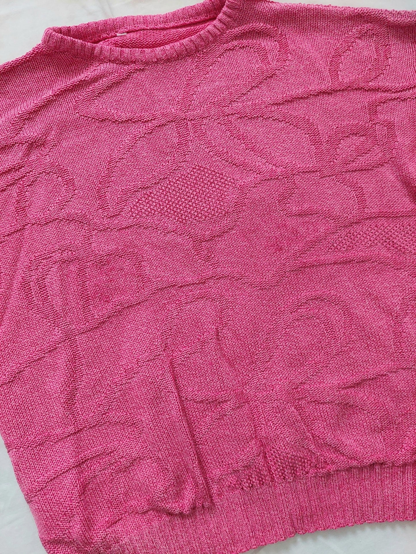 A  close up of the pink knitted sweater with unique swirly pattern 